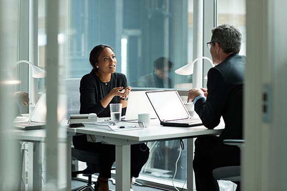 2 people talking at a table in an office 