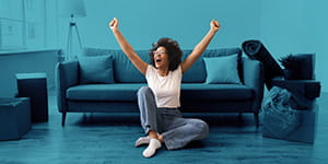 A woman sitting in front of a couch with her hand up in celebration