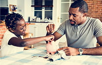 A man and his daughter adding coins to a piggy bank