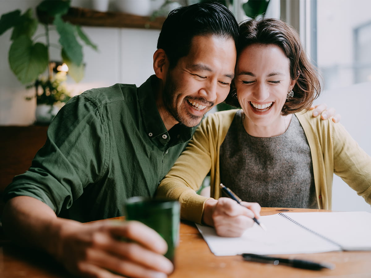 A couple smiling looking at bills together
