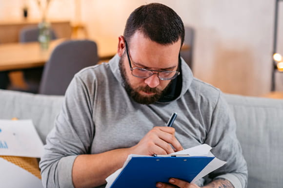 A man siting on the couch looking at debt consolidation. 