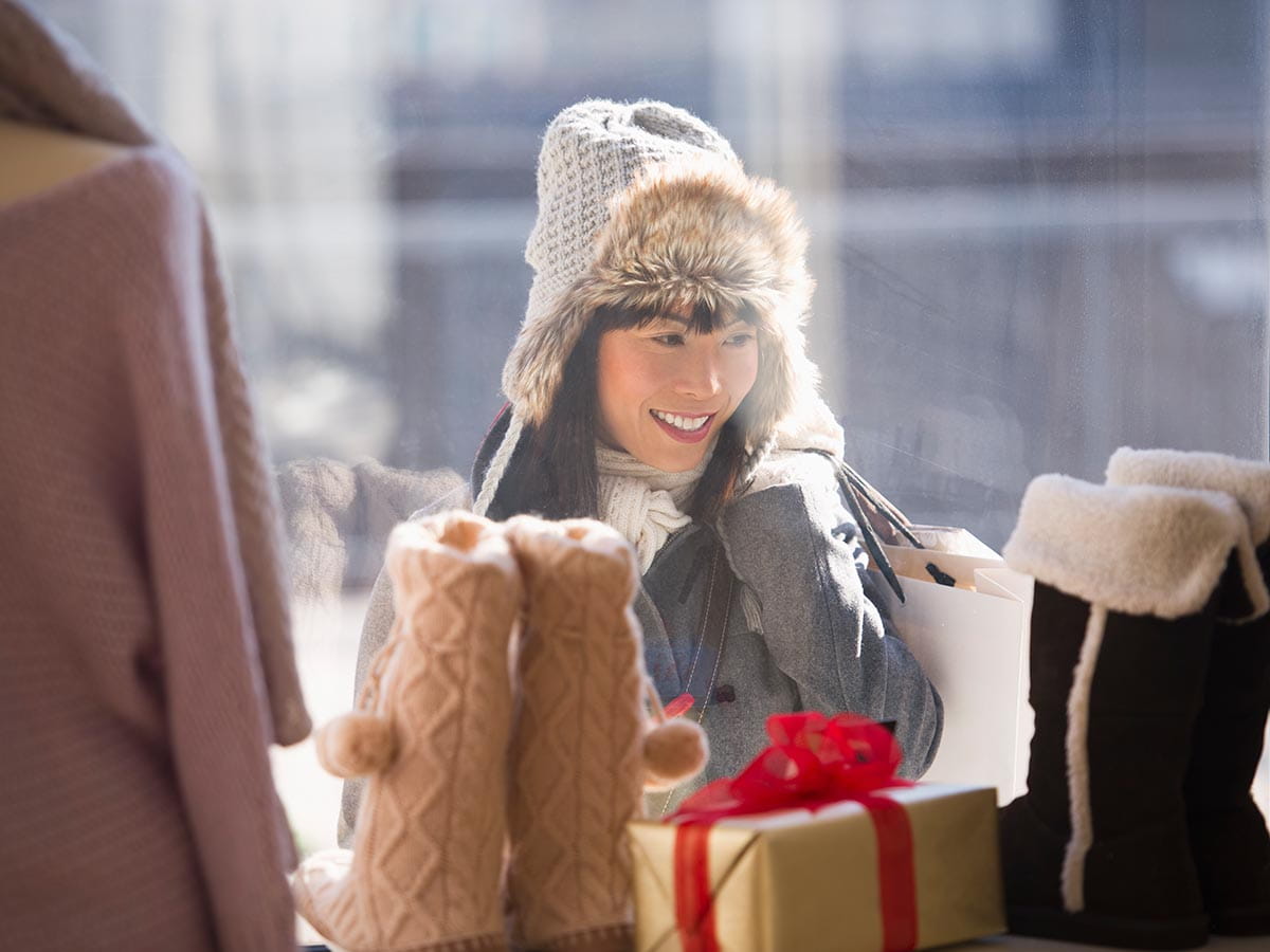 Woman outside a store window looking in holding a shopping bag