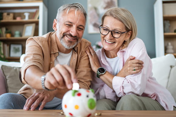 A couple sitting in their home adding money to a piggy bank