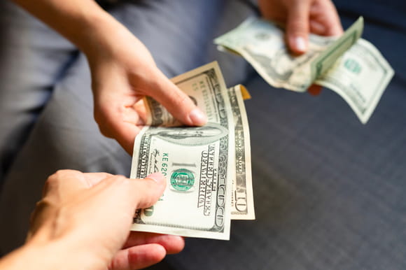 A hand places money in the hand of another. Lend money to friends and family. 