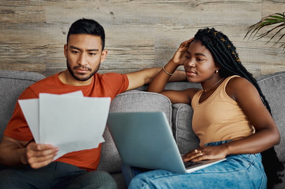 couple on couch reviewing documents and laptop. What to do if you think you might miss a payment.